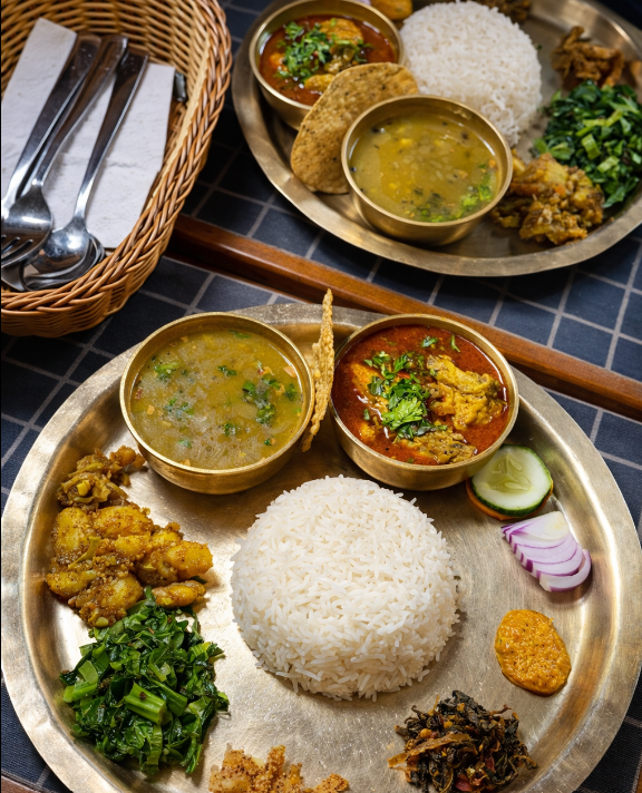 A brass thali of dal bhat with curry, greens and rice